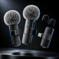 Three black wireless lapel microphones with gray furry windshields are shown floating above a dark surface on a black background. One microphone is clipped to a black collar, one is shown with a USB-C connector attached, and two foam windshields are displayed separately.